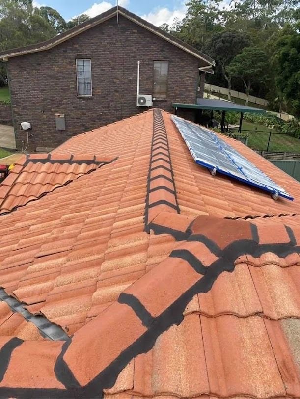 Roof with red tiles, black roof sealant lines, and a solar panel beside a brick house.