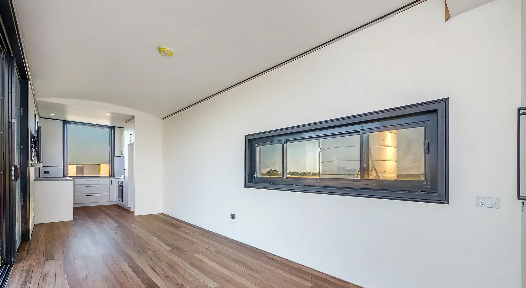 Empty modern room with wood flooring, white walls, and a large horizontal window overlooking a city view.