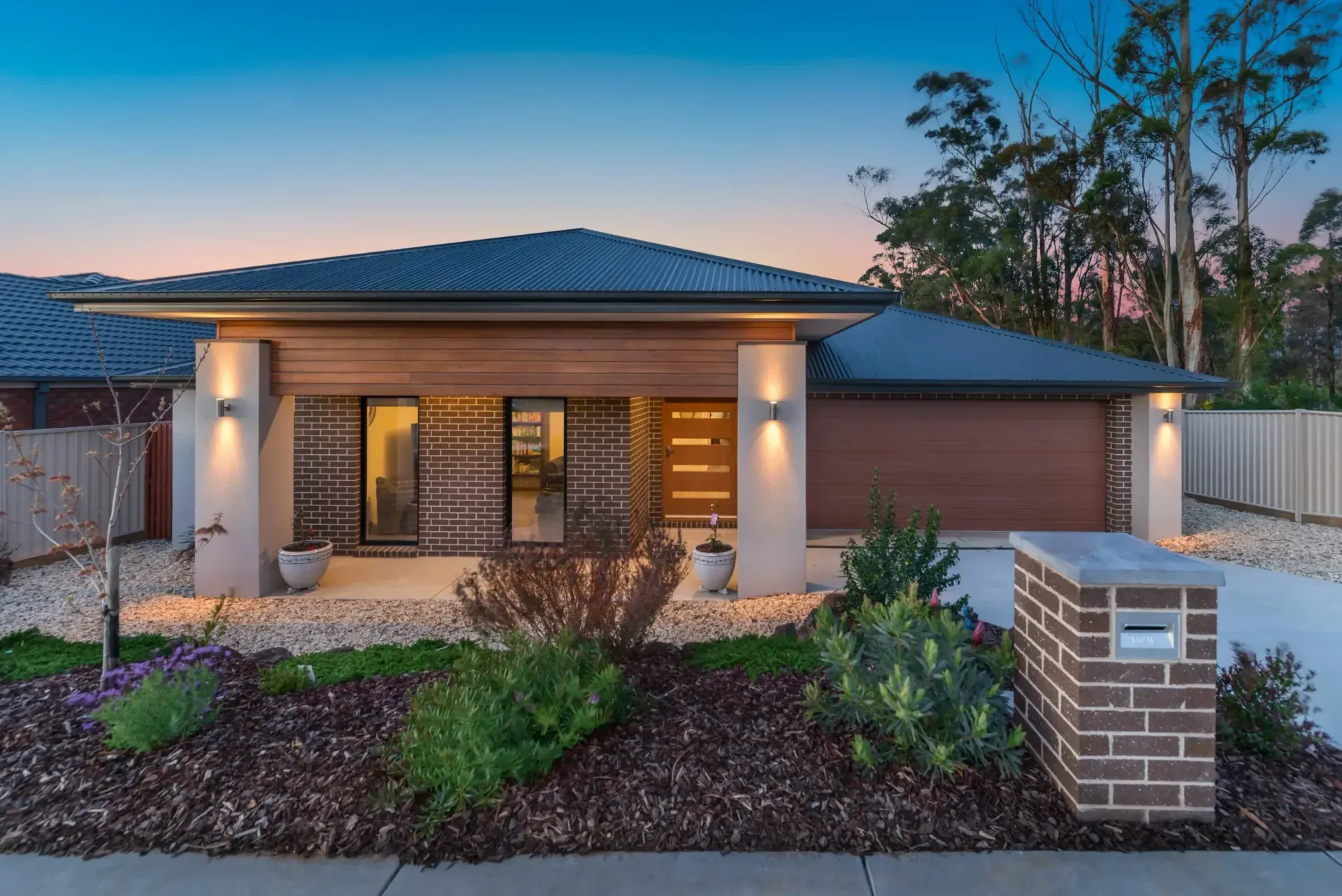 Modern single-story house with lit porch, brick mailbox, and desert landscaping at dusk