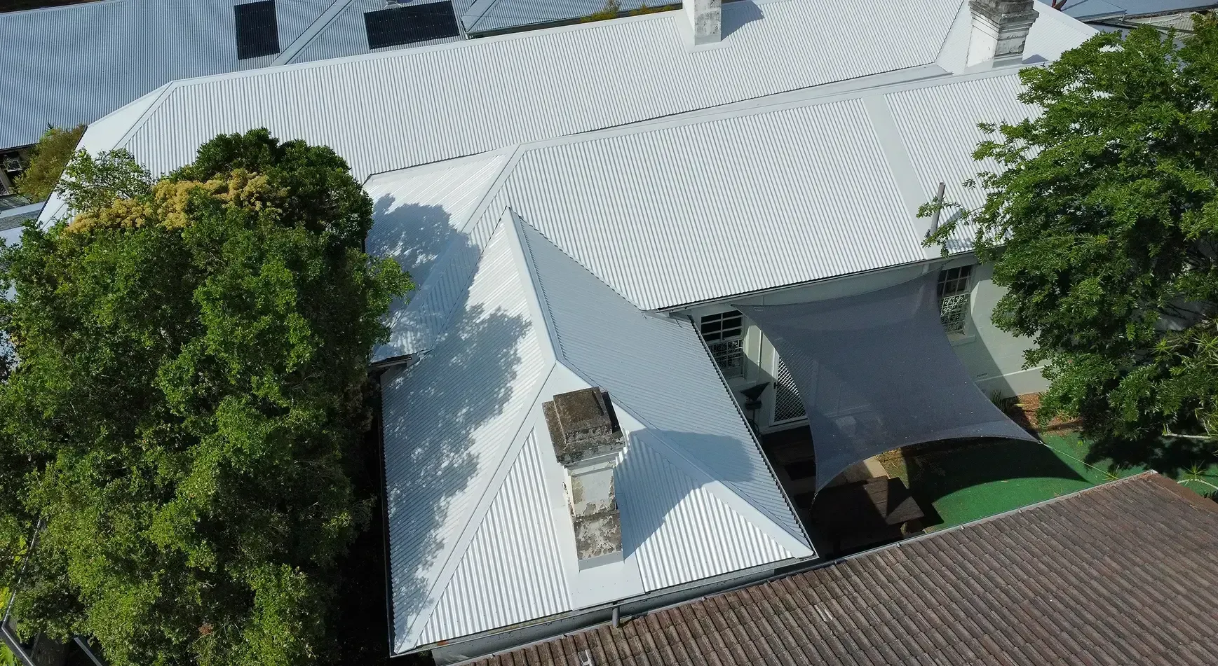 White metal rooftops beside a leafy green tree, seen from above.