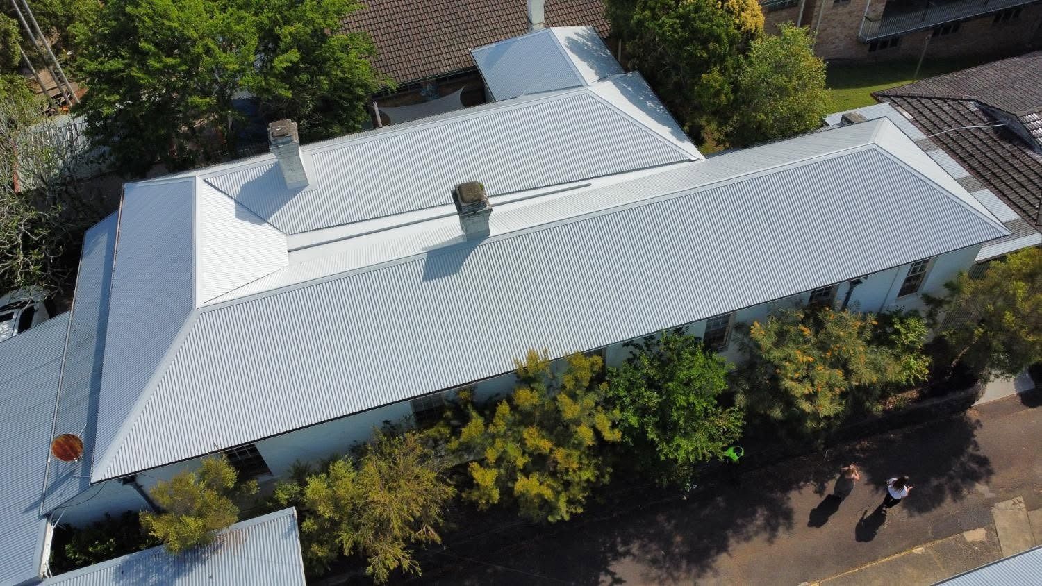 Aerial view of a white metal-roofed house surrounded by trees and neighboring homes.