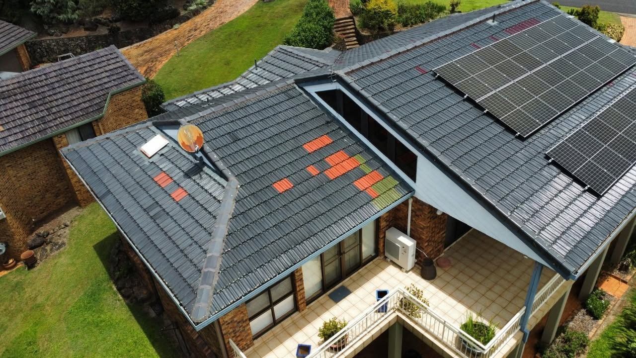 Aerial view of modern houses with dark roofs and rooftop solar panels, one roof being repaired.