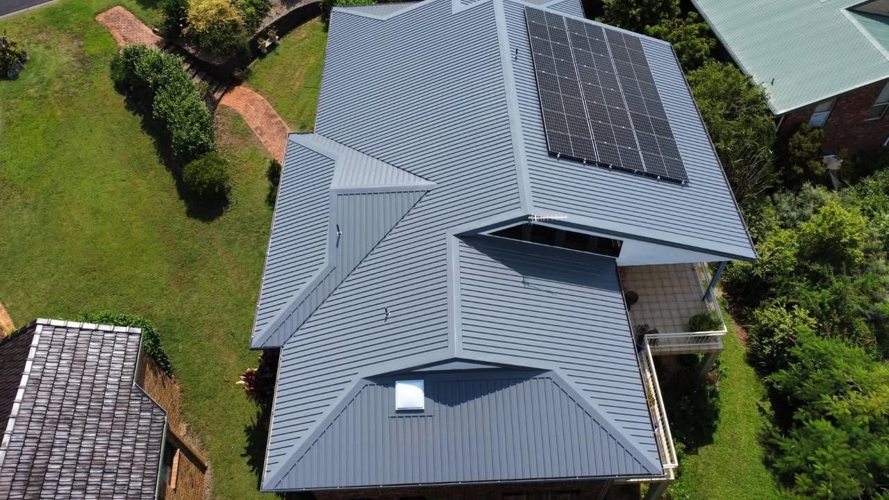 Aerial view of a house with a gray roof, solar panels, and surrounding green yard.