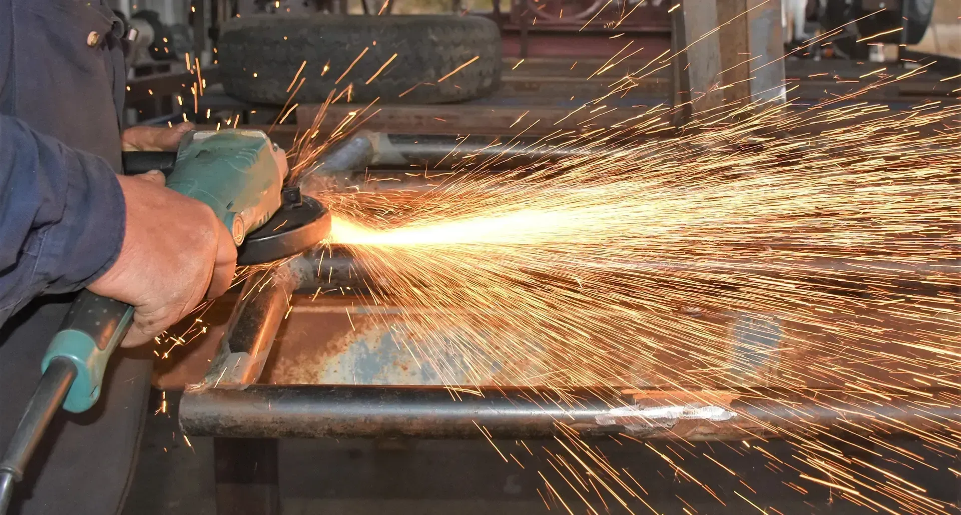 Worker using a green angle grinder to cut metal, sending bright sparks across a workshop table.