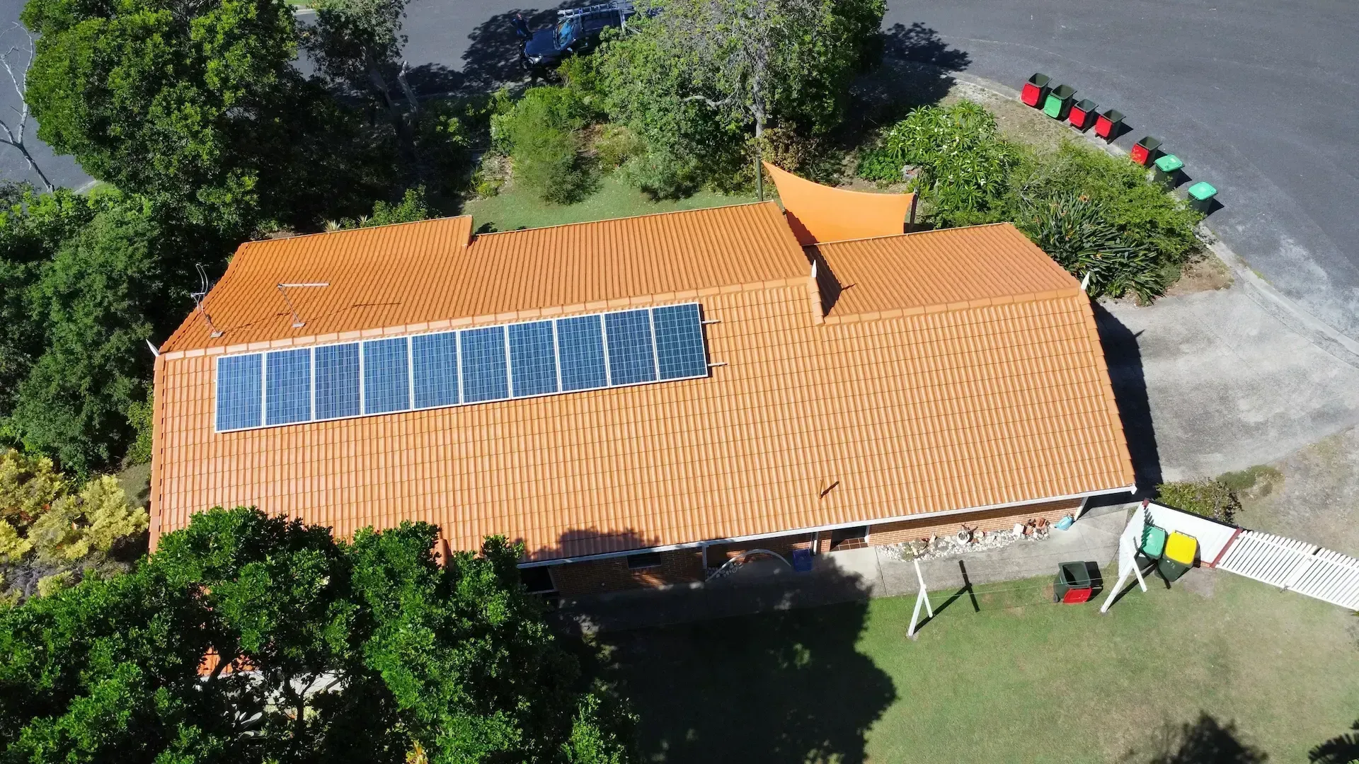 Aerial view of a house with orange roof and solar panels, surrounded by trees and yard.