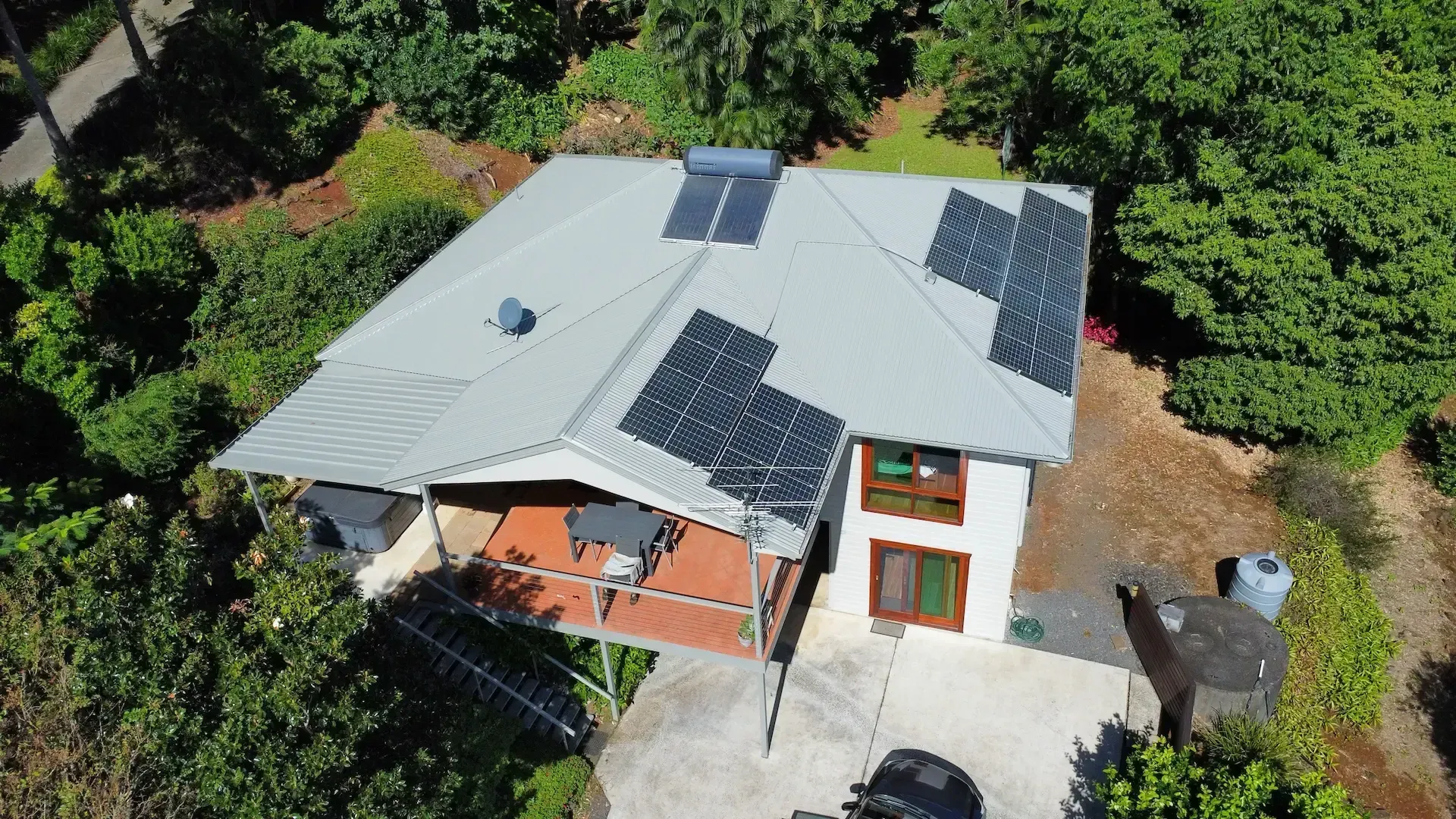 Aerial view of a white house with solar panels on the roof, surrounded by trees and a small front porch.