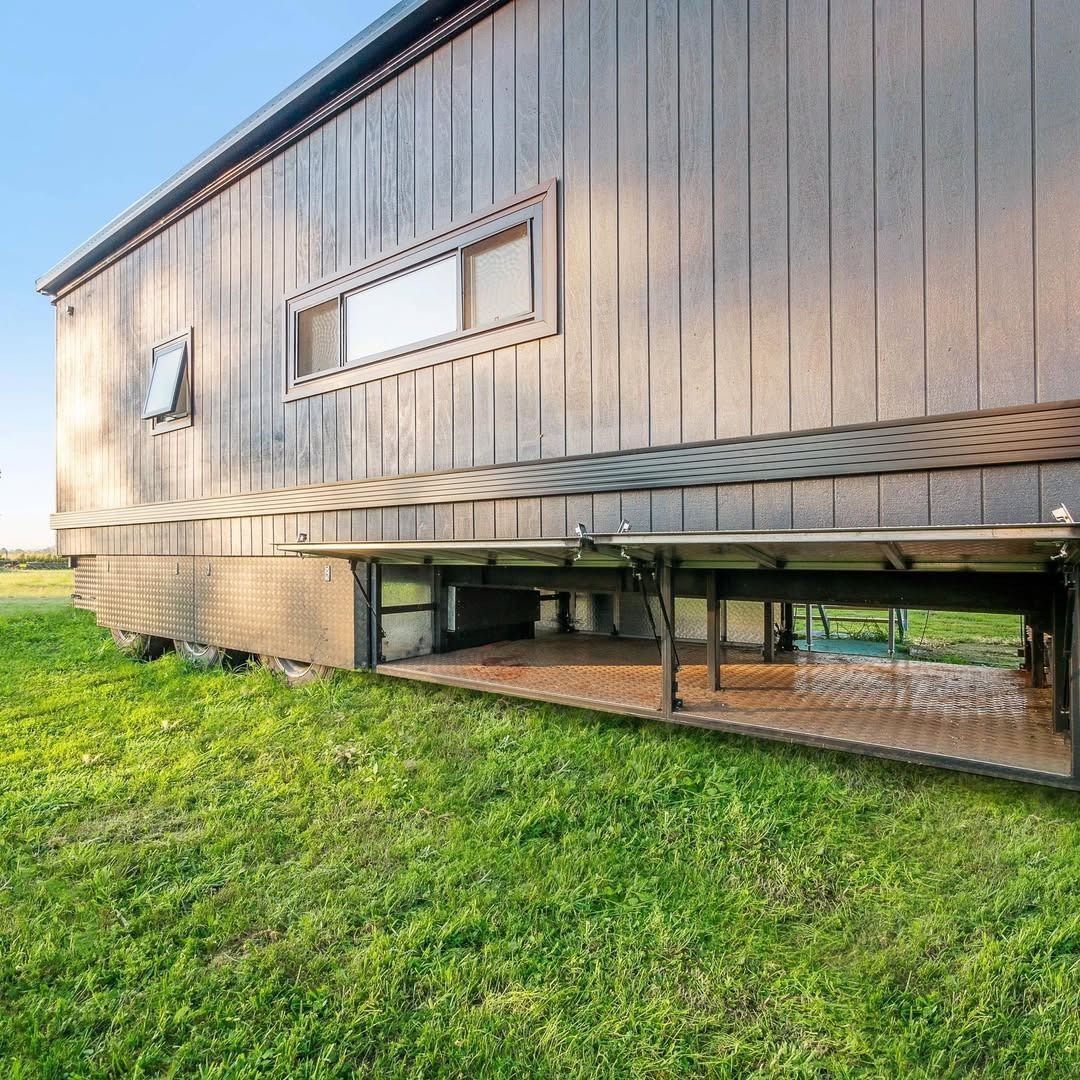 Modern tiny house on stilts with wooden siding and front porch in a grassy field at sunset