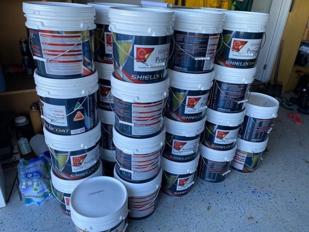 Stacks of white paint buckets in a storage area, with one empty bucket on the floor.