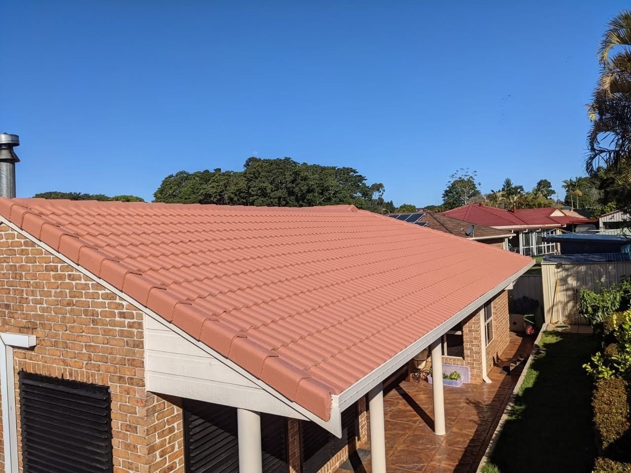 Red-tiled roof of a brick house with white trim under a clear blue sky
