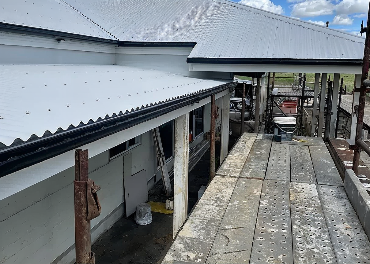 Damaged rooftop and weathered wooden walkway beside a white building under repair