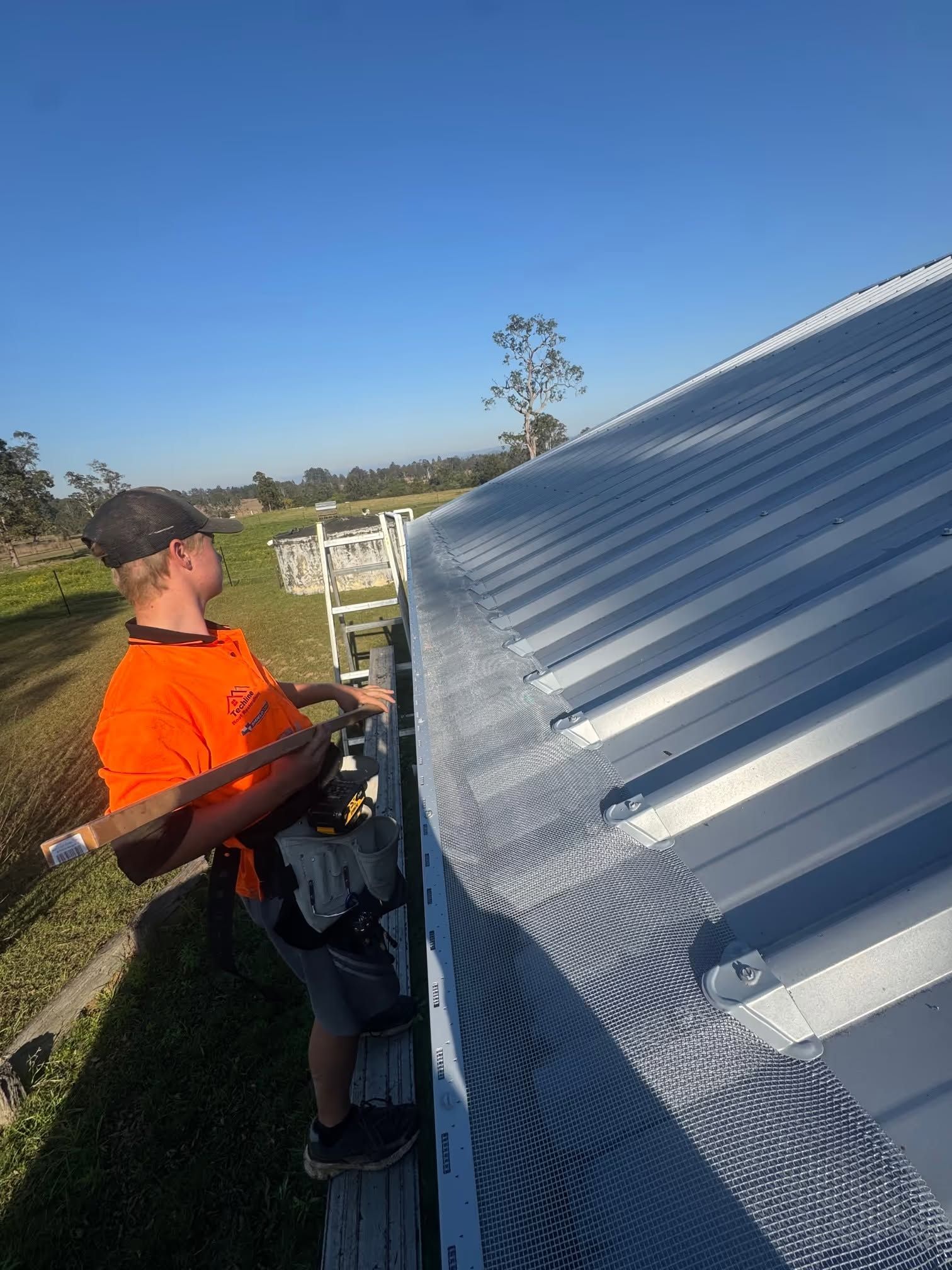 Worker installing metal roofing on a corrugated roof in bright sunlight