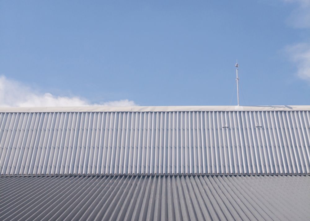 Corrugated metal roof under a clear blue sky with a thin antenna rising above it