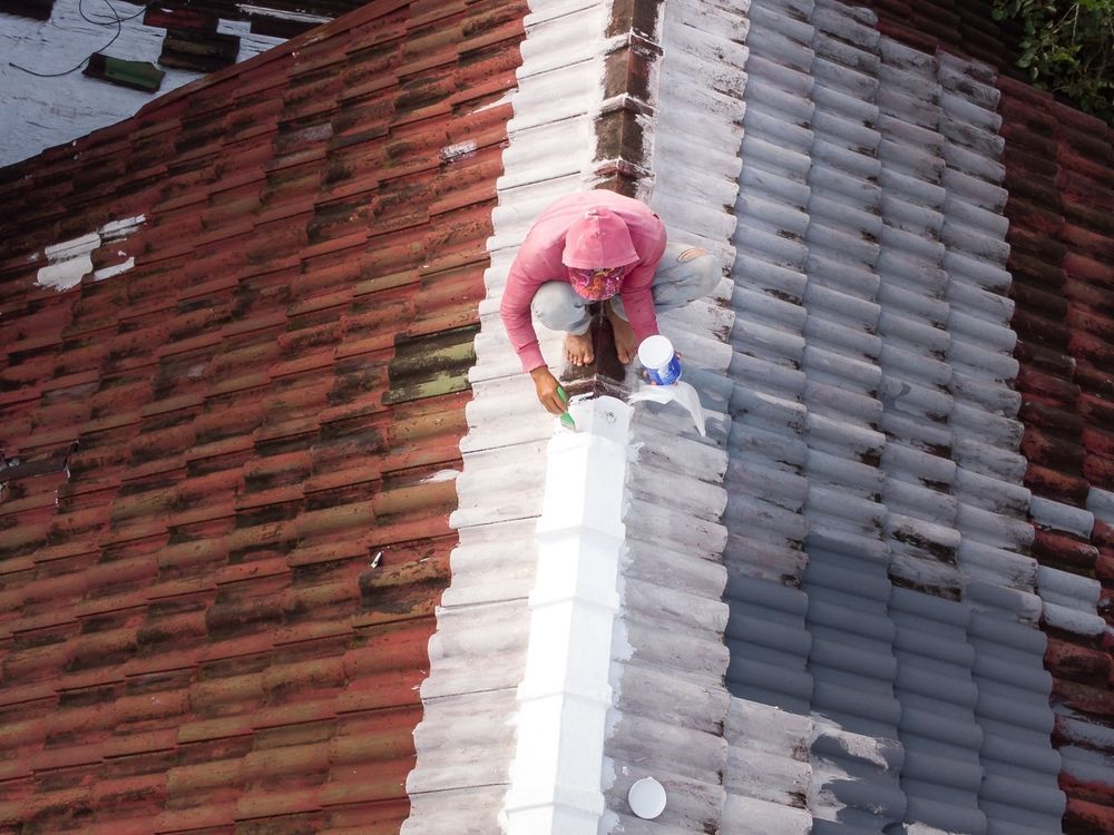 Worker in pink on a roof ridge painting a white stripe between red and gray roof tiles.
