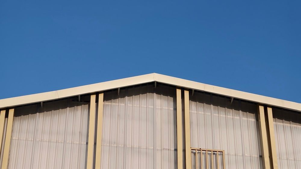 Low-angle view of a beige warehouse roof and wall against a clear blue sky