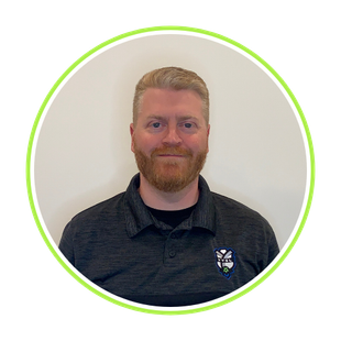 Portrait of a smiling person with short red hair and beard, wearing a dark shirt with a logo