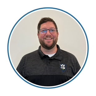 Smiling man in glasses and black polo shirt against a plain wall, framed in a blue circle.