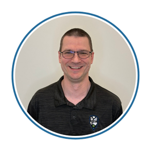 Smiling man with glasses in a dark polo shirt against a plain background.