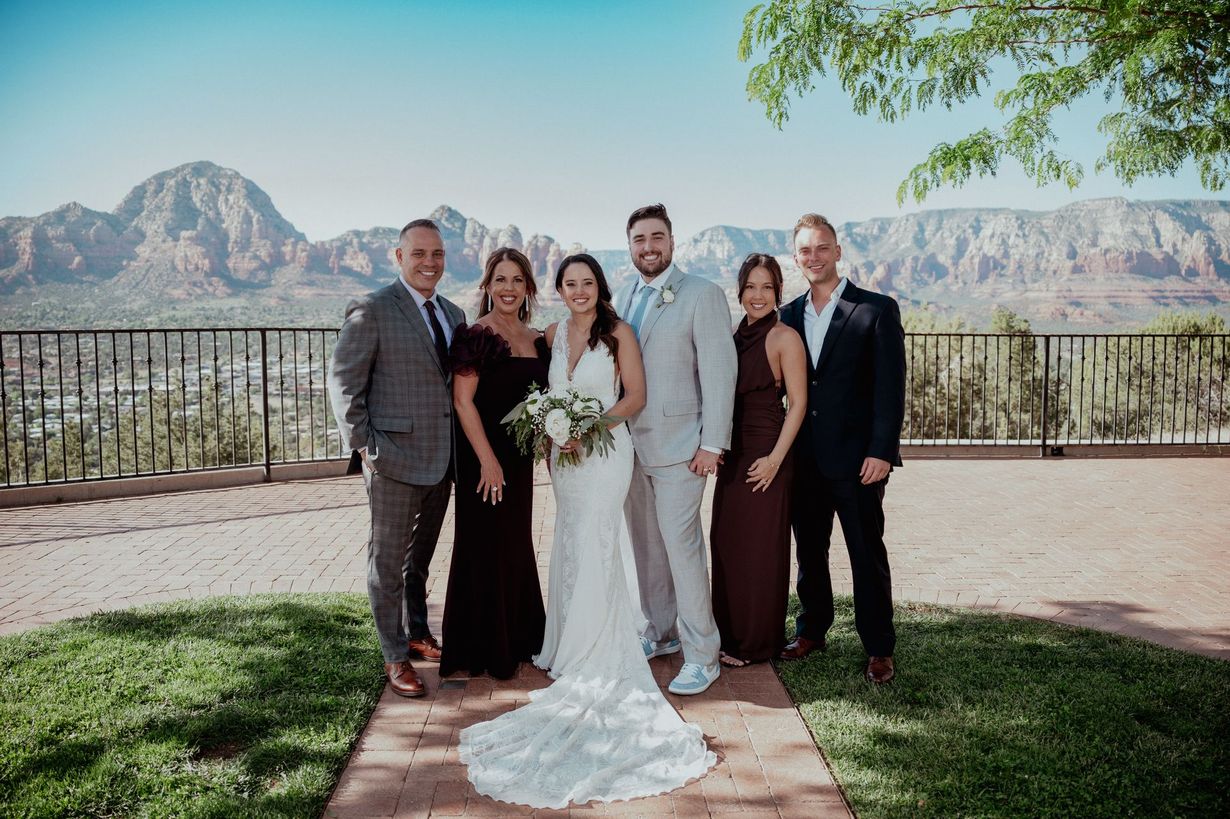 Wedding party posing outdoors with mountains in the background, bride holding bouquet in the center.