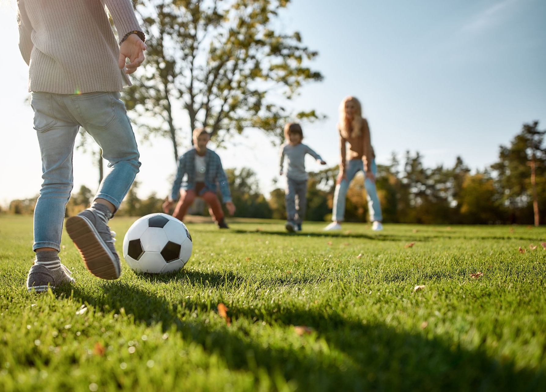 Child kicking a soccer ball in a park with family watching. Sunny day, green grass.
