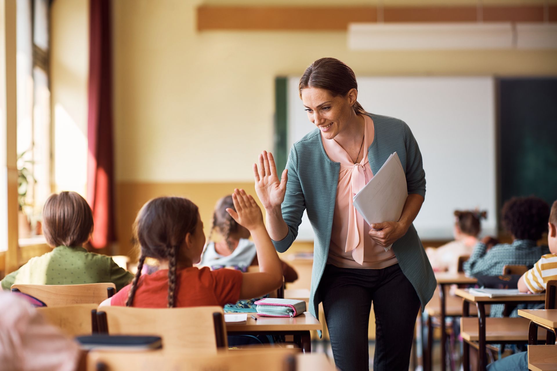 Children's classroom with teacher giving high-five to student.