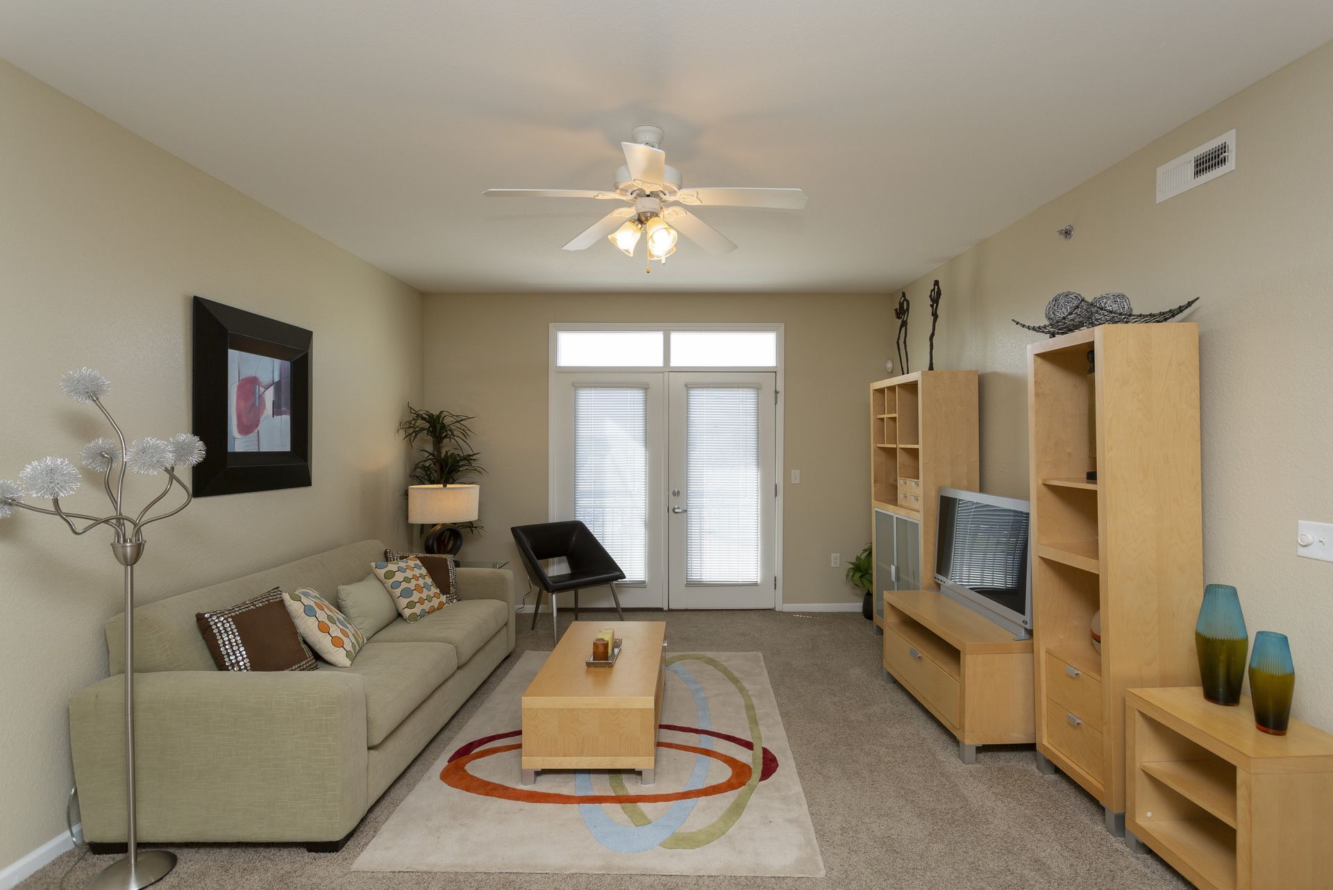 Living room with light-colored furniture, rug with circles, a couch, TV unit, and a doorway to a balcony.