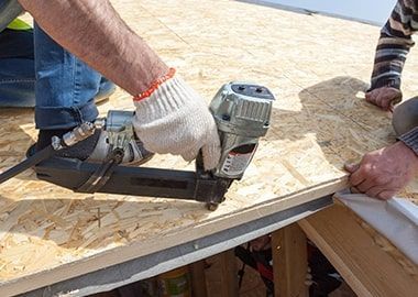 Des ouvriers fixent des panneaux de contreplaqué sur un toit à l'aide d'un cloueur pneumatique sur un chantier de construction.