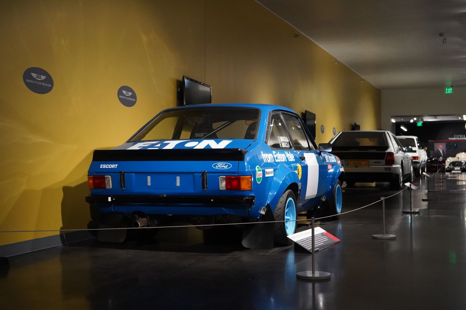 A row of cars and motorcycles are on display in a museum.