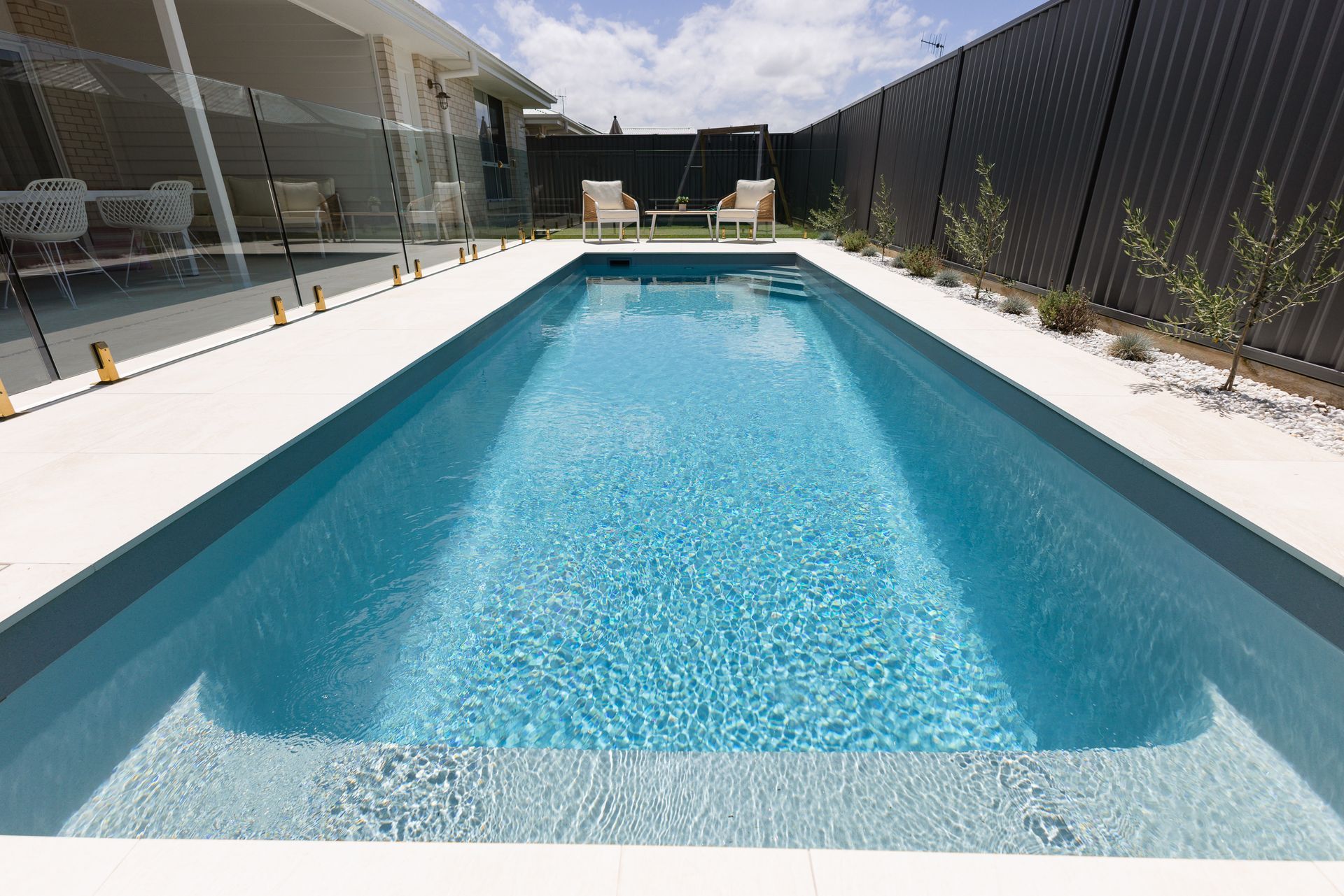 Rectangular Outdoor Swimming Pool with Blue Water Beside a House and Black Fence — New Vision Pools in Port Macquarie, NSW