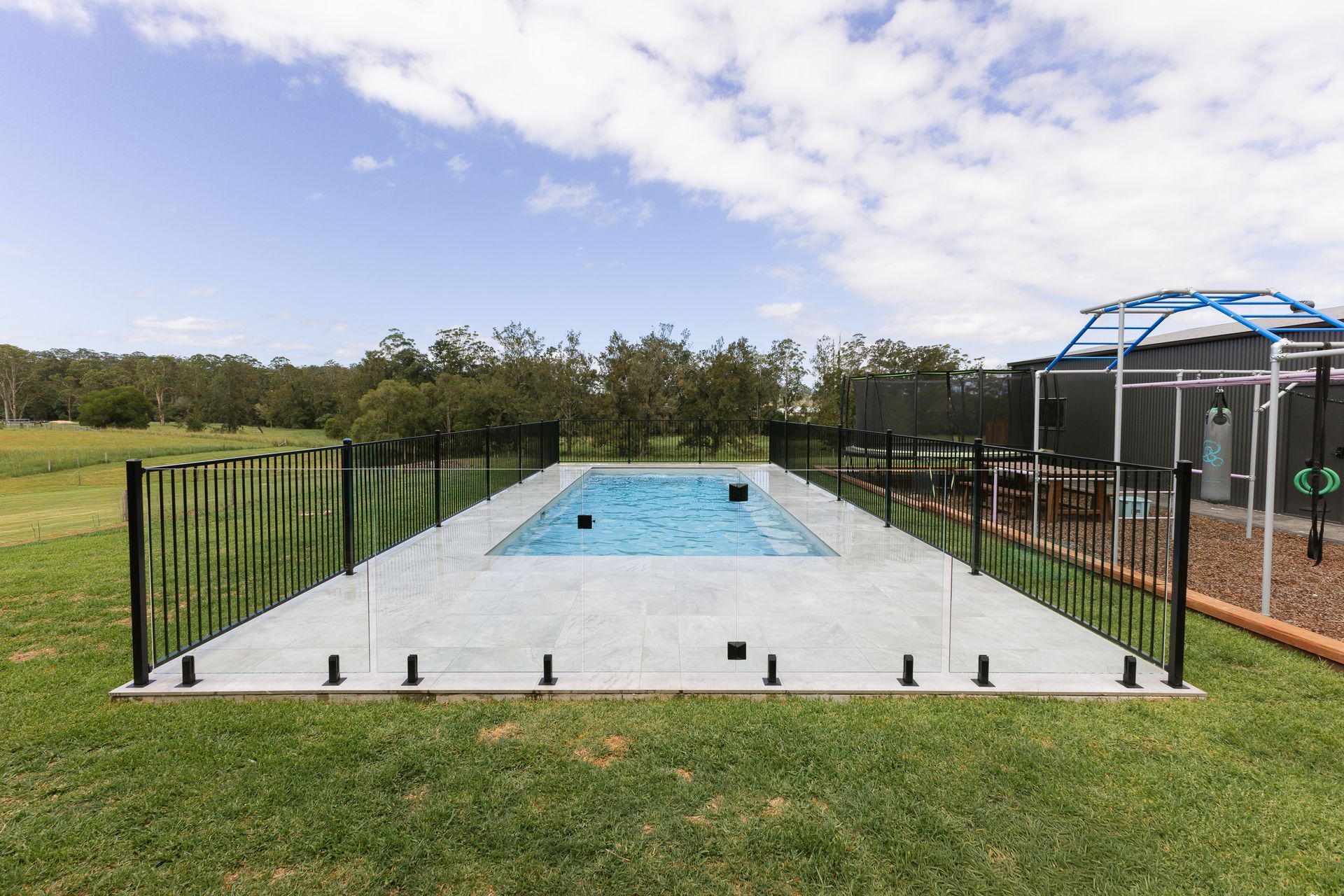 Backyard Pool Area with A Black Fence and A Screened Patio Beside a Grassy Yard — New Vision Pools in Port Macquarie, NSW