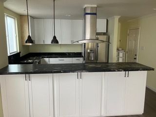 Empty kitchen with white cabinets, stainless steel refrigerator, and bright windowed dining area