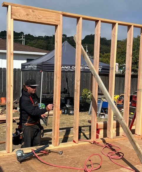 Partially framed wooden house under construction with lumber, tools, and workers on site