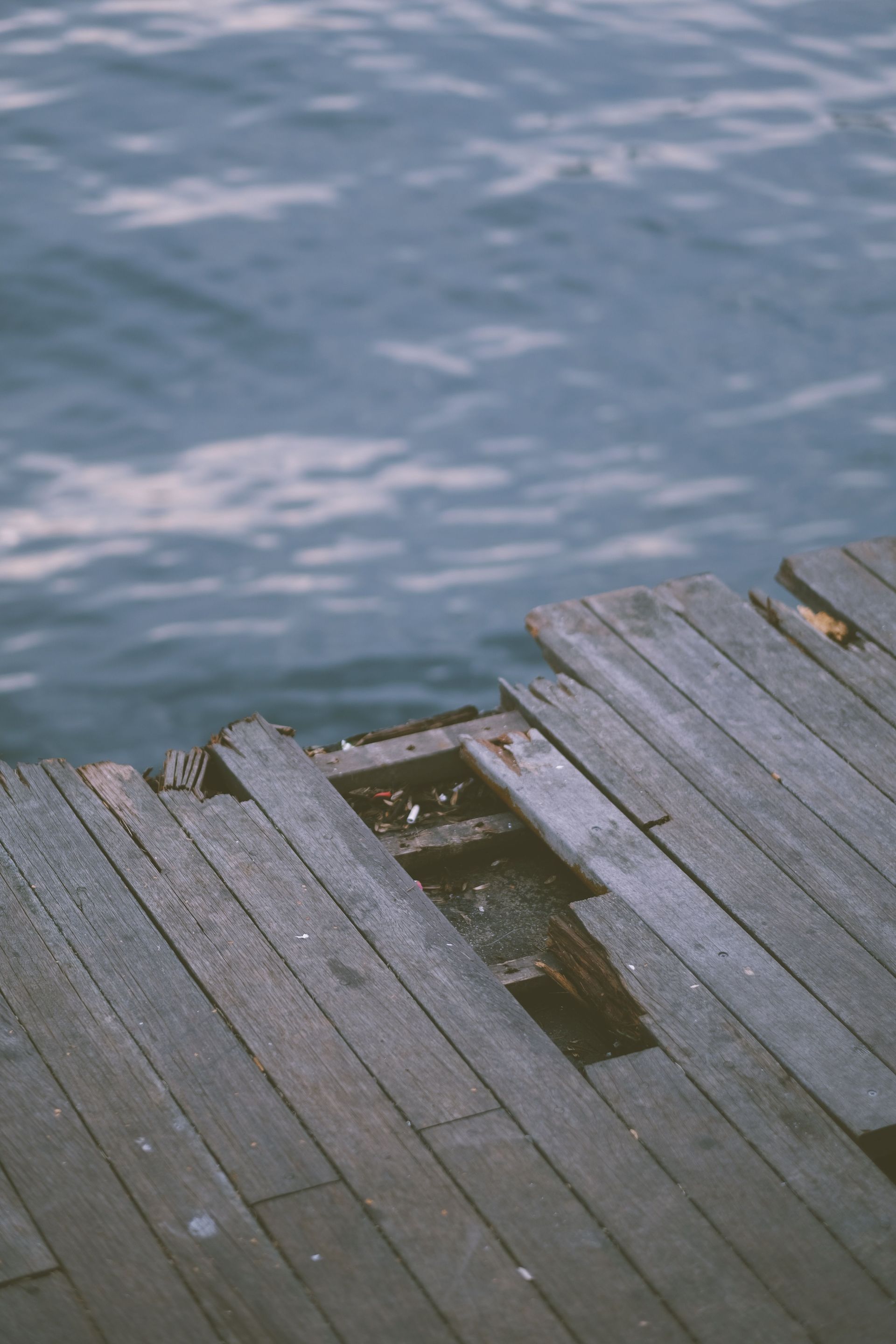 Weathered wooden dock beside rippling blue water, with a worn opening near the edge.