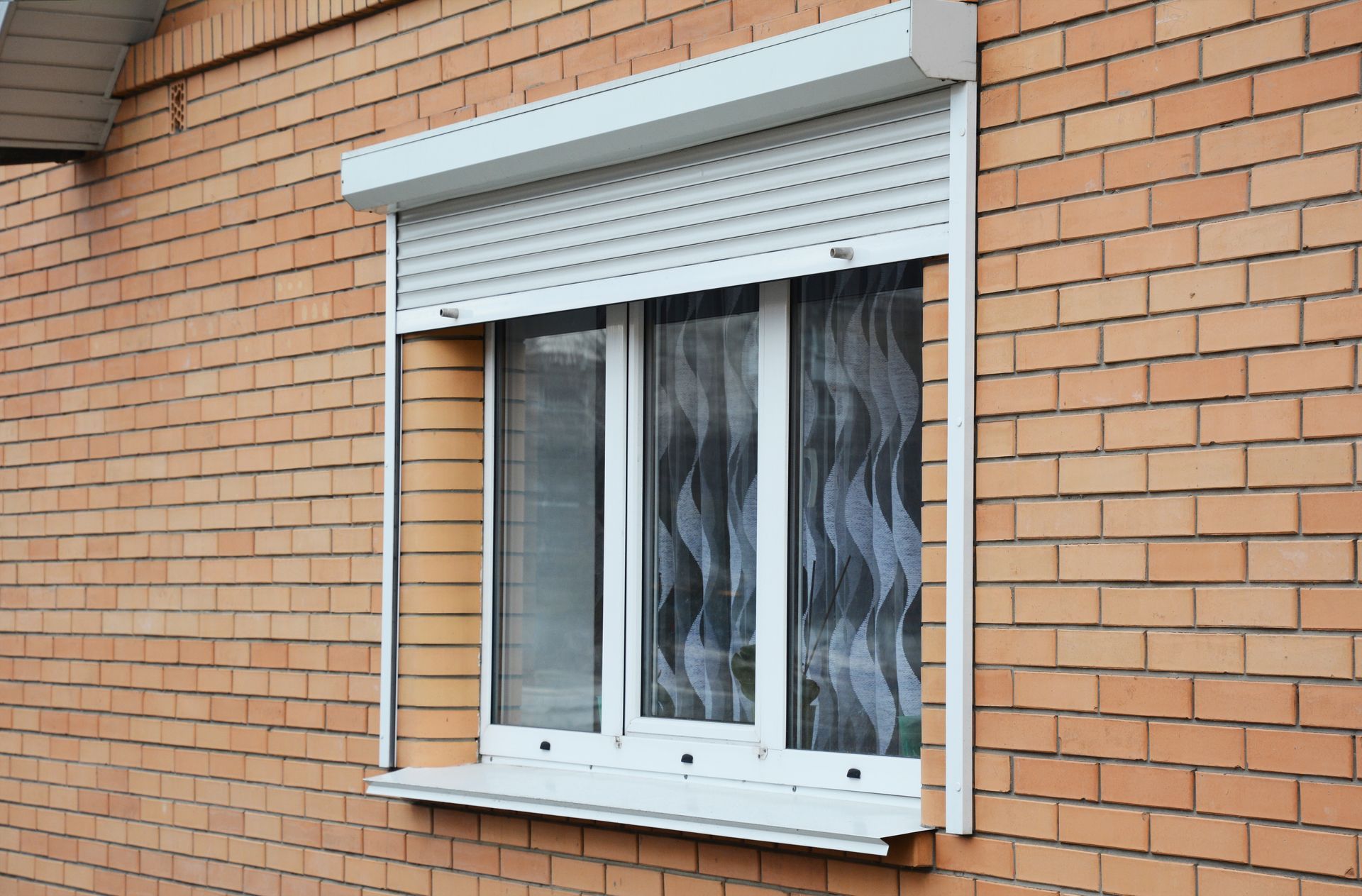 A brick wall with a window with a roller shutter on it.