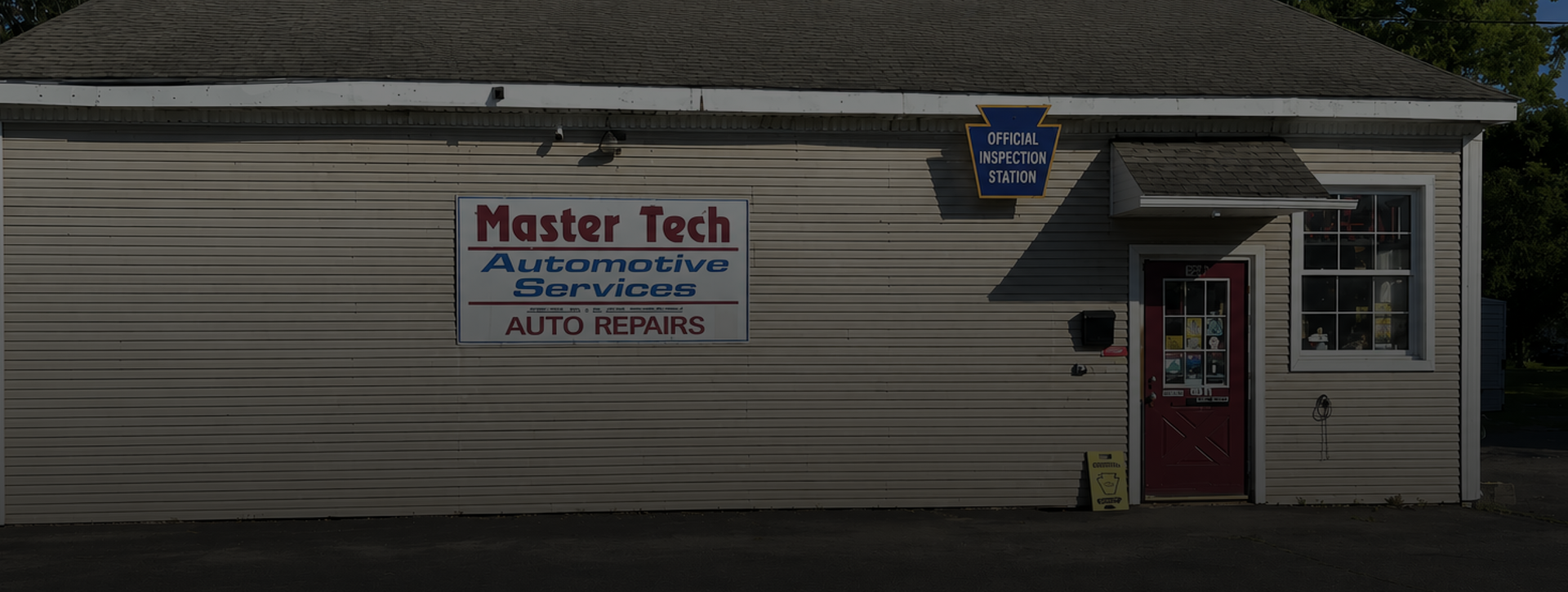 Master Tech Automotive sign on beige building beside a red door and black trash bin