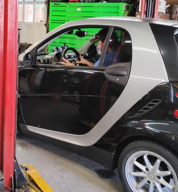 Our driver at the front seat of a black Smart Car ready to drive, parked in our garage | Master Tech Automotive Services