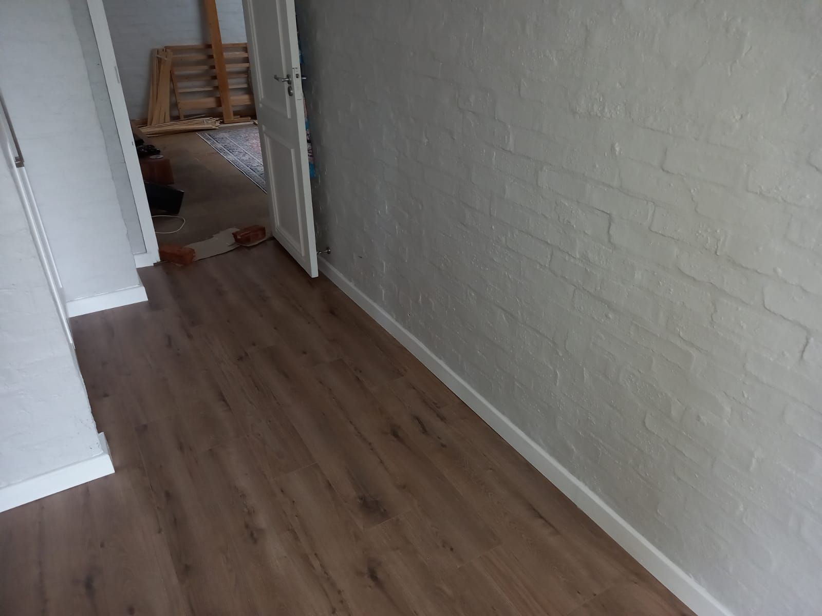 A hallway with a wooden floor and a white brick wall.