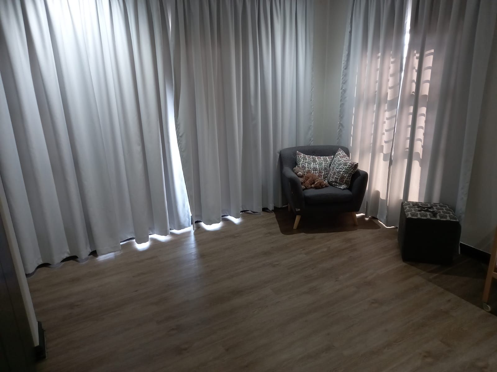 A living room with a chair and a window with white curtains.