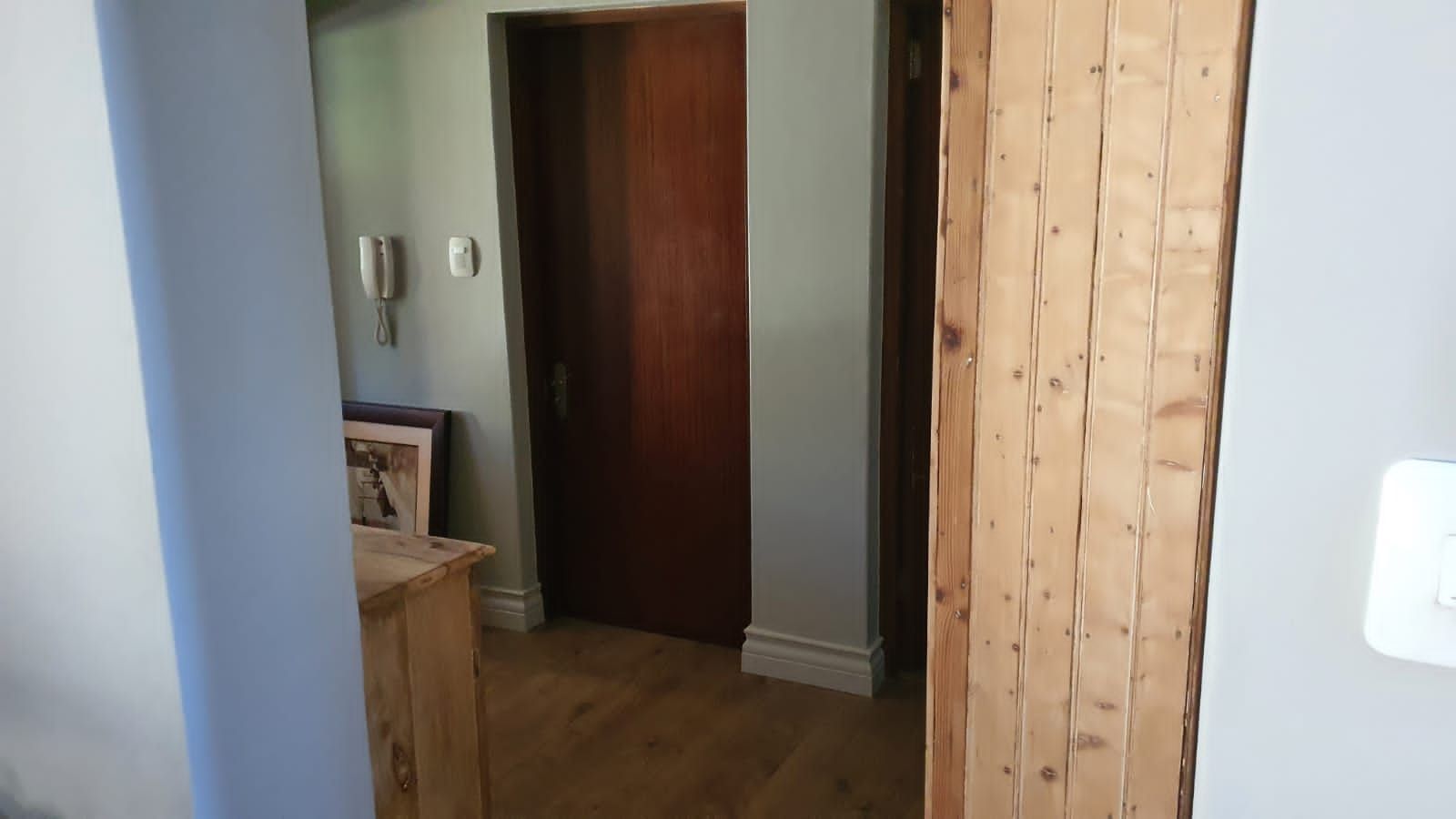 A hallway with a wooden door and a phone on the wall.