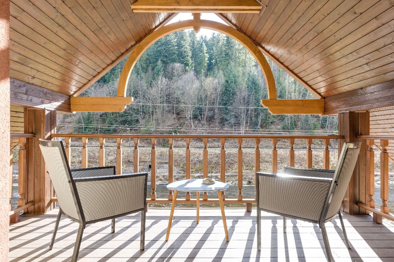 A balcony with two chairs and a table with a view of a forest.