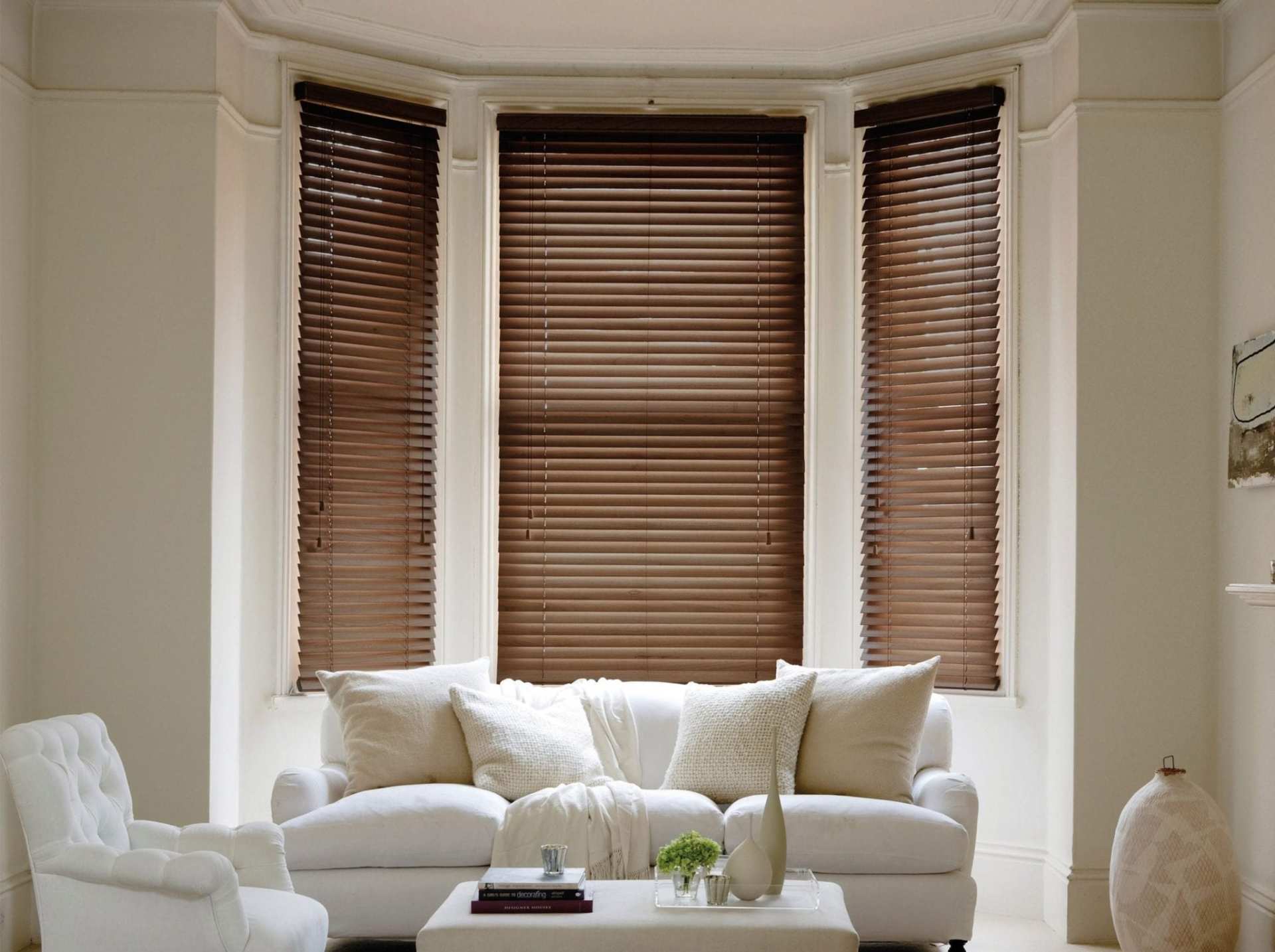 A living room with a couch , chair , coffee table and two windows with wooden blinds.