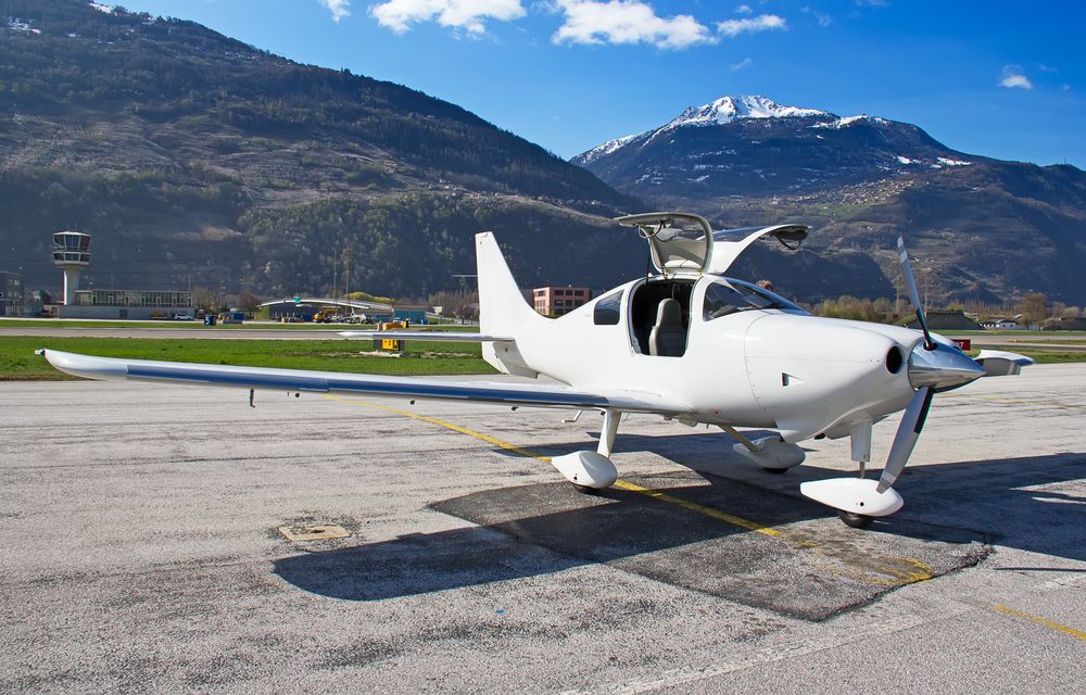 A Small White Plane is Parked on a Runway With Mountains in the Background — Strut Re-gas Mackay In Ooralea, QLD
