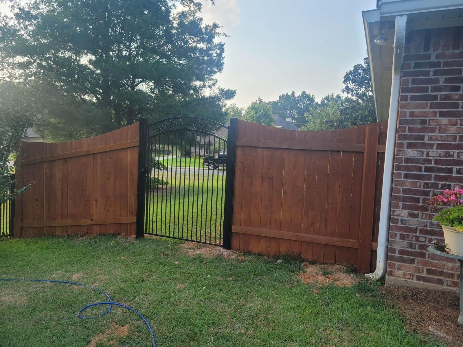A wooden fence with a metal gate in front of a brick house.