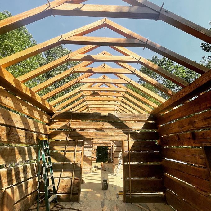 Partially built wooden roof frame inside a rustic shed, with sunlight and tools visible.