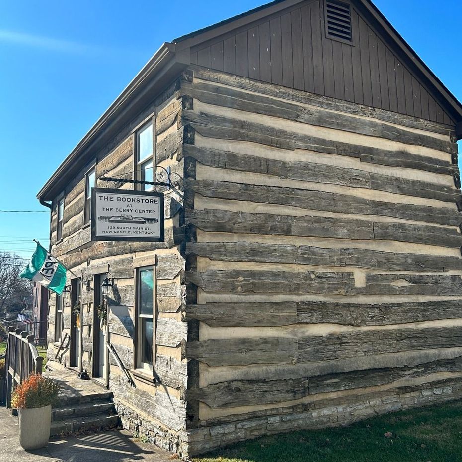 Rustic log cabin storefront with a sign, seen from the corner on a sunny day.