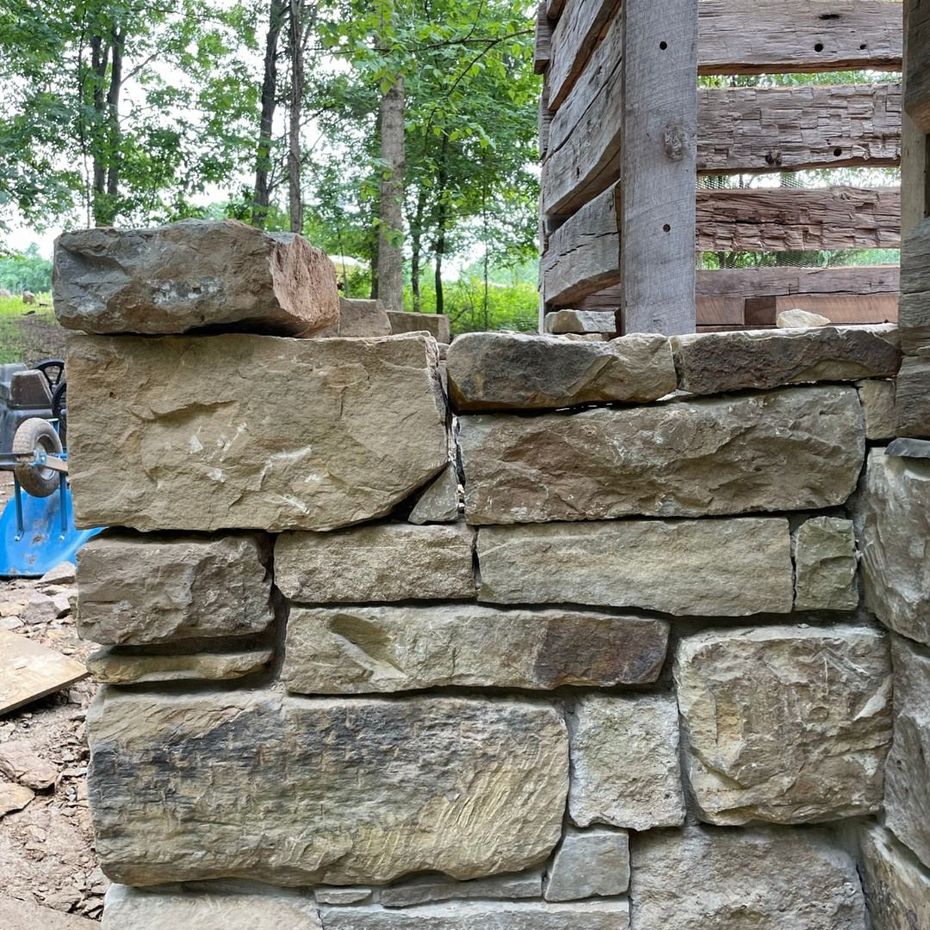 Stacked stone wall beside a wooden structure in a wooded outdoor setting