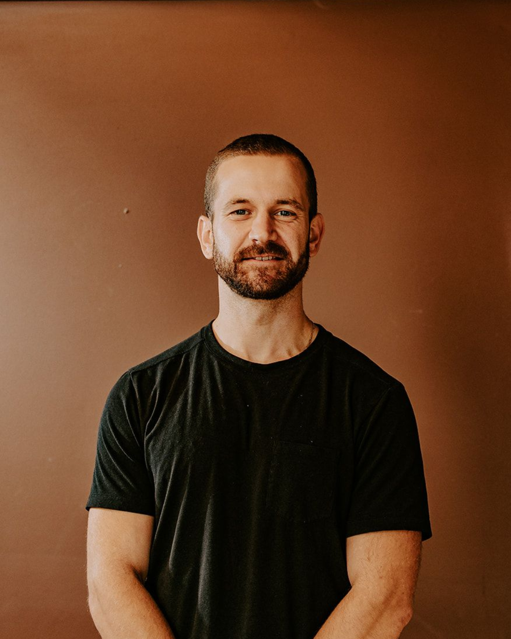 Smiling man in a black T-shirt standing against a brown wall