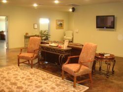 Living room with two orange chairs, a table, wall art, and a mounted TV on beige walls.