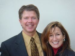 Two smiling people in business attire posing against a plain light background