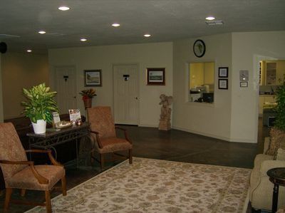 Quiet waiting room with chairs, patterned rug, wall art, and a plant near a reception table