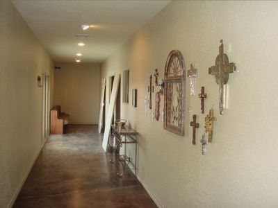 Narrow beige hallway with wall crosses, a small table, and recessed ceiling lights.